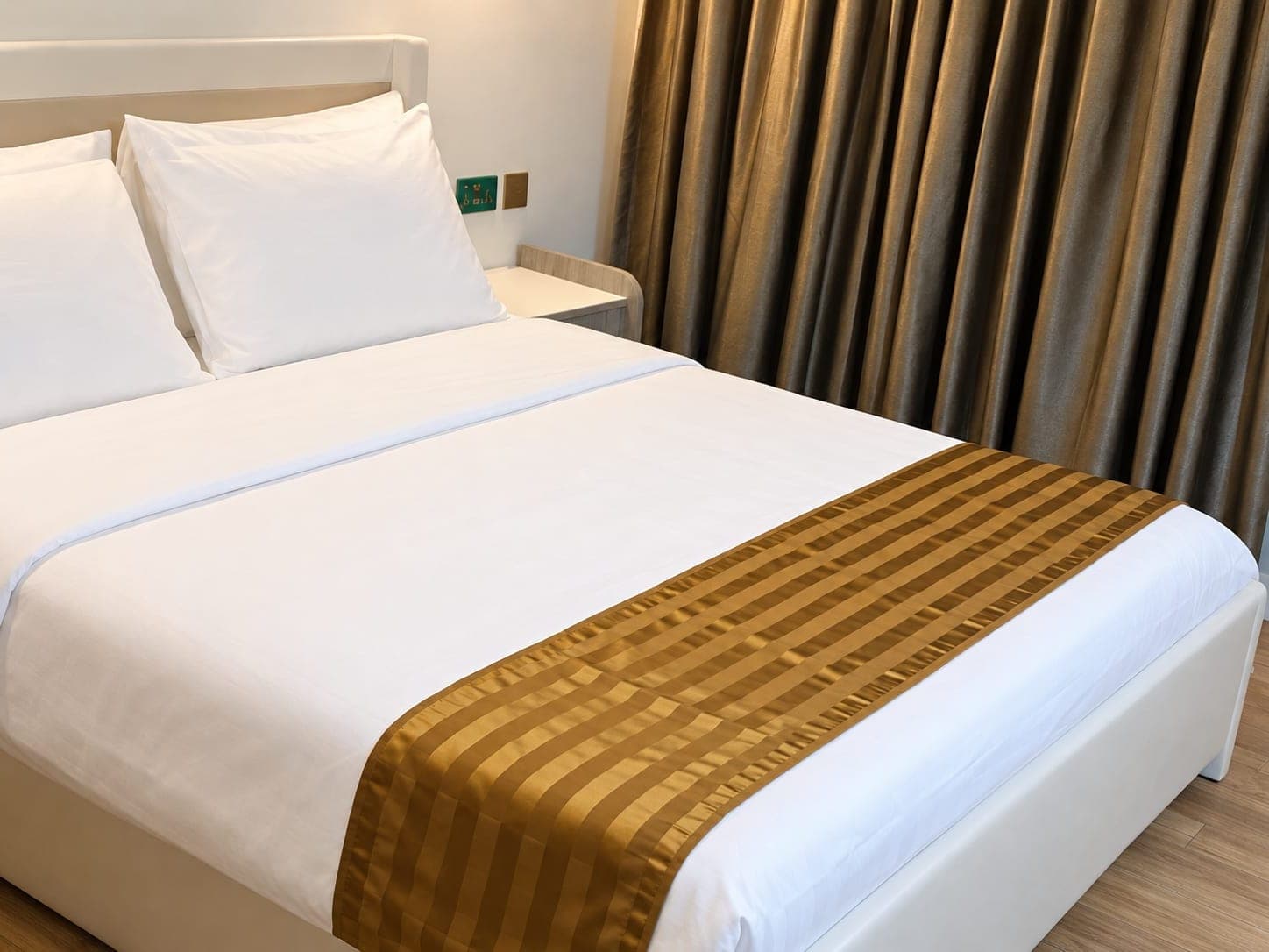 Deluxe Queen room with a gold runner, white linens and floor-length drapes